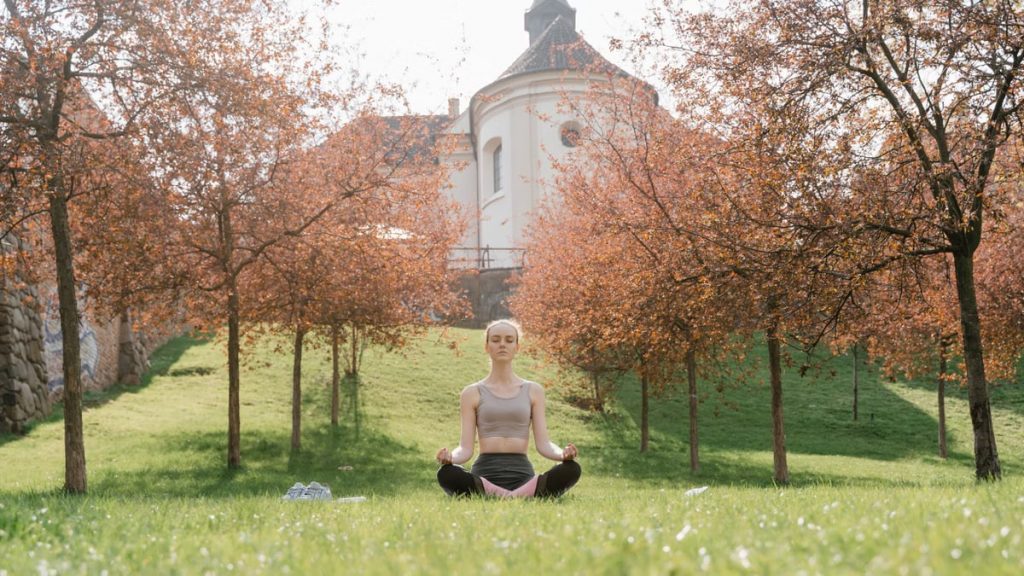 A woman practices meditation outdoors in a tranquil park during fall.