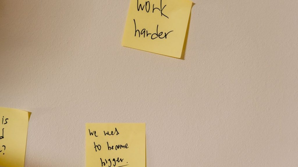 Yellow sticky notes with motivational phrases posted on a white wall, inspiring action.